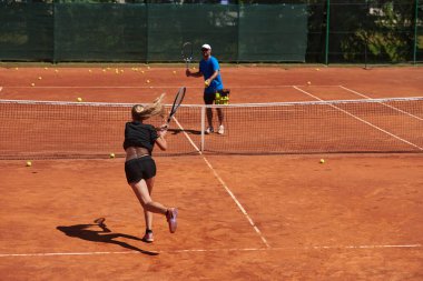 Profesyonel bir tenisçi ve onun koçu tenis kortunda güneşli bir günde antrenman yapıyorlar. Profesyonel bir tenisçinin antrenmanı ve hazırlığı.