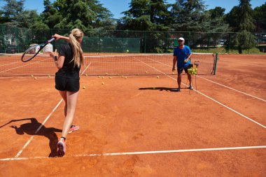 Profesyonel bir tenisçi ve onun koçu tenis kortunda güneşli bir günde antrenman yapıyorlar. Profesyonel bir tenisçinin antrenmanı ve hazırlığı.