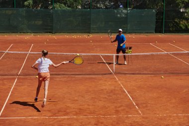 Profesyonel bir tenisçi ve onun koçu tenis kortunda güneşli bir günde antrenman yapıyorlar. Profesyonel bir tenisçinin antrenmanı ve hazırlığı.