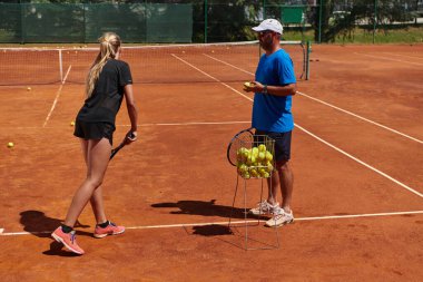 Profesyonel bir tenisçi ve onun koçu tenis kortunda güneşli bir günde antrenman yapıyorlar. Profesyonel bir tenisçinin antrenmanı ve hazırlığı.