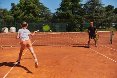 Profesyonel bir tenisçi ve onun koçu tenis kortunda güneşli bir günde antrenman yapıyorlar. Profesyonel bir tenisçinin antrenmanı ve hazırlığı.