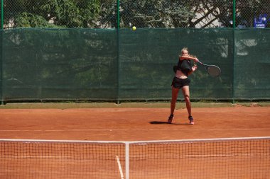 Güneşli bir günde tenis kortunun modern estetiğiyle çevrili profesyonel tenis yetenekleri sergileyen genç bir kız.