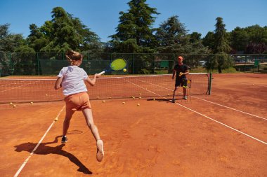 Profesyonel bir tenisçi ve onun koçu tenis kortunda güneşli bir günde antrenman yapıyorlar. Profesyonel bir tenisçinin antrenmanı ve hazırlığı.