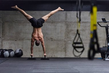 Amuda kalkmış kaslı bir adam, modern bir spor salonunda vücut dengesini ve gücünü arttırmak için çeşitli egzersizler yaparken olağanüstü denge ve vücut kontrolünü sergiliyor..