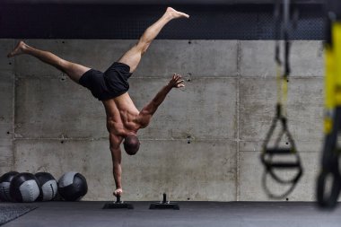 Amuda kalkmış kaslı bir adam, modern bir spor salonunda vücut dengesini ve gücünü arttırmak için çeşitli egzersizler yaparken olağanüstü denge ve vücut kontrolünü sergiliyor..