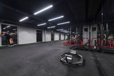 Çeşitli ekipmanlara sahip boş bir modern spor salonu, geniş, işlevsel ve iyi donanımlı bir eğitim tesisi sunuyor..