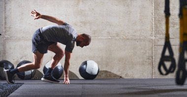 Modern bir spor salonuna atlayan kaslı bir adam, atletizm, güç ve kararlılığını yüksek yoğunluklu fitness rutiniyle sergiliyor..