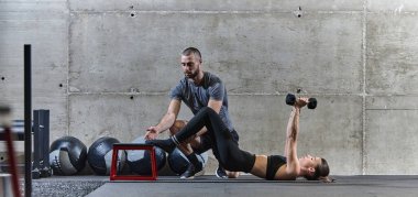 Modern bir spor salonunda formda bir kadına yardımcı olan kaslı bir adam çeşitli vücut egzersizleri ve kas esneklikleri yapıyor, fitness 'e olan bağlılıklarını gösteriyor ve takım çalışmasından faydalanıyor ve destek oluyor..