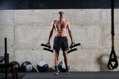 Kaslı bir adam modern bir spor salonunda omuz egzersizi yapar. Gücünü ve kendini spora adadığını gösterir.