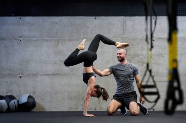 Modern bir spor salonunda formda bir kadına yardımcı olan kaslı bir adam çeşitli vücut egzersizleri ve kas esneklikleri yapıyor, fitness 'e olan bağlılıklarını gösteriyor ve takım çalışmasından faydalanıyor ve destek oluyor..