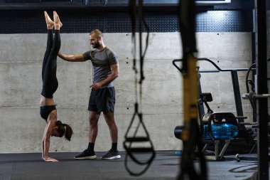 Modern bir spor salonunda formda bir kadına yardımcı olan kaslı bir adam çeşitli vücut egzersizleri ve kas esneklikleri yapıyor, fitness 'e olan bağlılıklarını gösteriyor ve takım çalışmasından faydalanıyor ve destek oluyor..