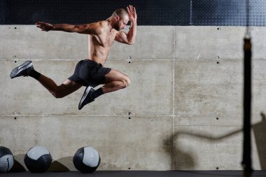 Modern bir spor salonuna atlayan kaslı bir adam, atletizm, güç ve kararlılığını yüksek yoğunluklu fitness rutiniyle sergiliyor..