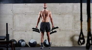 Kaslı bir adam modern bir spor salonunda omuz egzersizi yapar. Gücünü ve kendini spora adadığını gösterir.