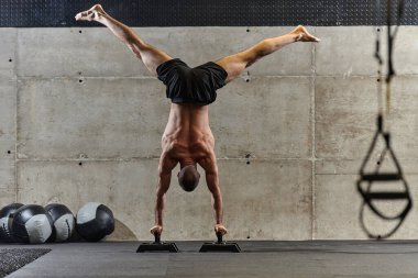 Amuda kalkmış kaslı bir adam, modern bir spor salonunda vücut dengesini ve gücünü arttırmak için çeşitli egzersizler yaparken olağanüstü denge ve vücut kontrolünü sergiliyor..