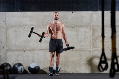 Kaslı bir adam modern bir spor salonunda omuz egzersizi yapar. Gücünü ve kendini spora adadığını gösterir.
