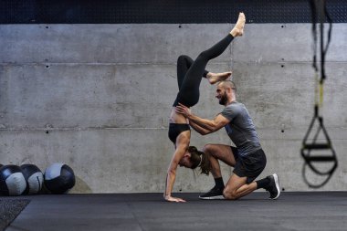 Modern bir spor salonunda formda bir kadına yardımcı olan kaslı bir adam çeşitli vücut egzersizleri ve kas esneklikleri yapıyor, fitness 'e olan bağlılıklarını gösteriyor ve takım çalışmasından faydalanıyor ve destek oluyor..