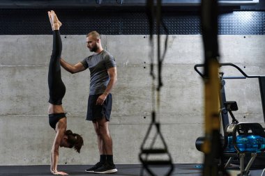 Modern bir spor salonunda formda bir kadına yardımcı olan kaslı bir adam çeşitli vücut egzersizleri ve kas esneklikleri yapıyor, fitness 'e olan bağlılıklarını gösteriyor ve takım çalışmasından faydalanıyor ve destek oluyor..