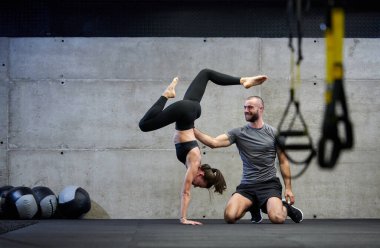 Modern bir spor salonunda formda bir kadına yardımcı olan kaslı bir adam çeşitli vücut egzersizleri ve kas esneklikleri yapıyor, fitness 'e olan bağlılıklarını gösteriyor ve takım çalışmasından faydalanıyor ve destek oluyor..