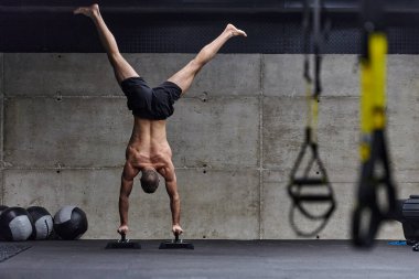 Amuda kalkmış kaslı bir adam, modern bir spor salonunda vücut dengesini ve gücünü arttırmak için çeşitli egzersizler yaparken olağanüstü denge ve vücut kontrolünü sergiliyor..