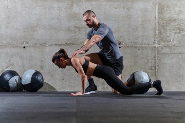 Modern bir spor salonunda formda bir kadına yardımcı olan kaslı bir adam çeşitli vücut egzersizleri ve kas esneklikleri yapıyor, fitness 'e olan bağlılıklarını gösteriyor ve takım çalışmasından faydalanıyor ve destek oluyor..