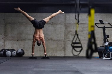 Amuda kalkmış kaslı bir adam, modern bir spor salonunda vücut dengesini ve gücünü arttırmak için çeşitli egzersizler yaparken olağanüstü denge ve vücut kontrolünü sergiliyor..