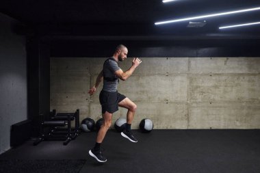 Modern bir spor salonuna atlayan kaslı bir adam, atletizm, güç ve kararlılığını yüksek yoğunluklu fitness rutiniyle sergiliyor..