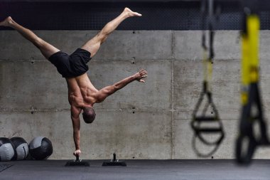Amuda kalkmış kaslı bir adam, modern bir spor salonunda vücut dengesini ve gücünü arttırmak için çeşitli egzersizler yaparken olağanüstü denge ve vücut kontrolünü sergiliyor..