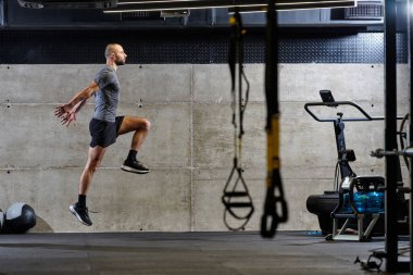 Modern bir spor salonuna atlayan kaslı bir adam, atletizm, güç ve kararlılığını yüksek yoğunluklu fitness rutiniyle sergiliyor..