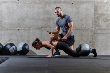 Modern bir spor salonunda formda bir kadına yardımcı olan kaslı bir adam çeşitli vücut egzersizleri ve kas esneklikleri yapıyor, fitness 'e olan bağlılıklarını gösteriyor ve takım çalışmasından faydalanıyor ve destek oluyor..