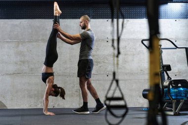 Modern bir spor salonunda formda bir kadına yardımcı olan kaslı bir adam çeşitli vücut egzersizleri ve kas esneklikleri yapıyor, fitness 'e olan bağlılıklarını gösteriyor ve takım çalışmasından faydalanıyor ve destek oluyor..