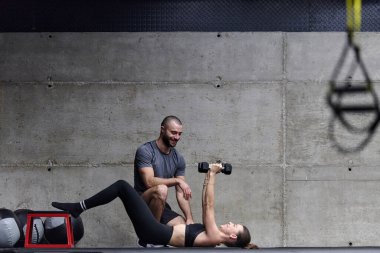 Modern bir spor salonunda formda bir kadına yardımcı olan kaslı bir adam çeşitli vücut egzersizleri ve kas esneklikleri yapıyor, fitness 'e olan bağlılıklarını gösteriyor ve takım çalışmasından faydalanıyor ve destek oluyor..