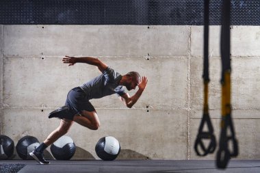 Modern bir spor salonuna atlayan kaslı bir adam, atletizm, güç ve kararlılığını yüksek yoğunluklu fitness rutiniyle sergiliyor..