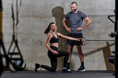 Modern bir spor salonunda formda bir kadına yardımcı olan kaslı bir adam çeşitli vücut egzersizleri ve kas esneklikleri yapıyor, fitness 'e olan bağlılıklarını gösteriyor ve takım çalışmasından faydalanıyor ve destek oluyor..