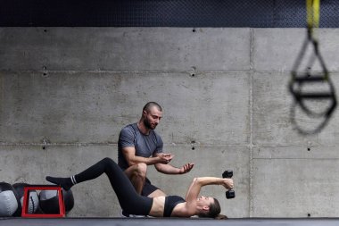 Modern bir spor salonunda formda bir kadına yardımcı olan kaslı bir adam çeşitli vücut egzersizleri ve kas esneklikleri yapıyor, fitness 'e olan bağlılıklarını gösteriyor ve takım çalışmasından faydalanıyor ve destek oluyor..