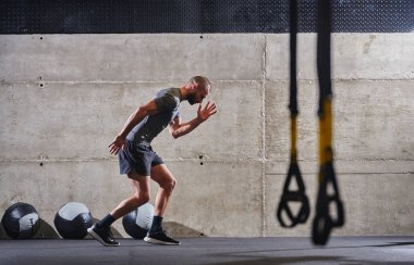 Modern bir spor salonuna atlayan kaslı bir adam, atletizm, güç ve kararlılığını yüksek yoğunluklu fitness rutiniyle sergiliyor..