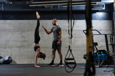 Modern bir spor salonunda formda bir kadına yardımcı olan kaslı bir adam çeşitli vücut egzersizleri ve kas esneklikleri yapıyor, fitness 'e olan bağlılıklarını gösteriyor ve takım çalışmasından faydalanıyor ve destek oluyor..
