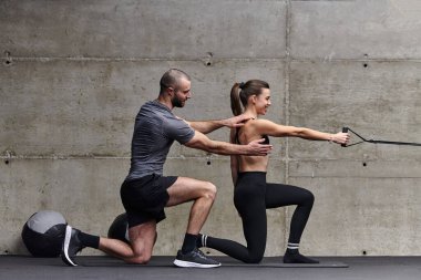 Modern bir spor salonunda formda bir kadına yardımcı olan kaslı bir adam çeşitli vücut egzersizleri ve kas esneklikleri yapıyor, fitness 'e olan bağlılıklarını gösteriyor ve takım çalışmasından faydalanıyor ve destek oluyor..