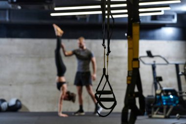 Modern bir spor salonunda formda bir kadına yardımcı olan kaslı bir adam çeşitli vücut egzersizleri ve kas esneklikleri yapıyor, fitness 'e olan bağlılıklarını gösteriyor ve takım çalışmasından faydalanıyor ve destek oluyor..
