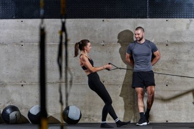Modern bir spor salonunda formda bir kadına yardımcı olan kaslı bir adam çeşitli vücut egzersizleri ve kas esneklikleri yapıyor, fitness 'e olan bağlılıklarını gösteriyor ve takım çalışmasından faydalanıyor ve destek oluyor..