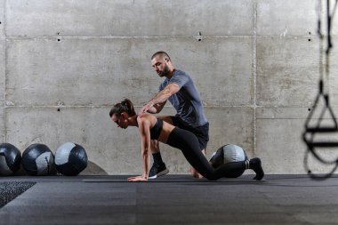 Modern bir spor salonunda formda bir kadına yardımcı olan kaslı bir adam çeşitli vücut egzersizleri ve kas esneklikleri yapıyor, fitness 'e olan bağlılıklarını gösteriyor ve takım çalışmasından faydalanıyor ve destek oluyor..