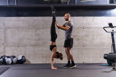 Modern bir spor salonunda formda bir kadına yardımcı olan kaslı bir adam çeşitli vücut egzersizleri ve kas esneklikleri yapıyor, fitness 'e olan bağlılıklarını gösteriyor ve takım çalışmasından faydalanıyor ve destek oluyor..