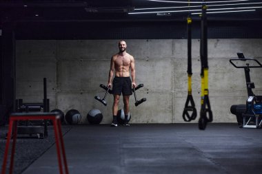 Kaslı bir adam modern bir spor salonunda omuz egzersizi yapar. Gücünü ve kendini spora adadığını gösterir.