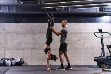 Modern bir spor salonunda formda bir kadına yardımcı olan kaslı bir adam çeşitli vücut egzersizleri ve kas esneklikleri yapıyor, fitness 'e olan bağlılıklarını gösteriyor ve takım çalışmasından faydalanıyor ve destek oluyor..