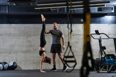 Modern bir spor salonunda formda bir kadına yardımcı olan kaslı bir adam çeşitli vücut egzersizleri ve kas esneklikleri yapıyor, fitness 'e olan bağlılıklarını gösteriyor ve takım çalışmasından faydalanıyor ve destek oluyor..