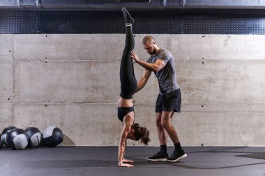 Modern bir spor salonunda formda bir kadına yardımcı olan kaslı bir adam çeşitli vücut egzersizleri ve kas esneklikleri yapıyor, fitness 'e olan bağlılıklarını gösteriyor ve takım çalışmasından faydalanıyor ve destek oluyor..