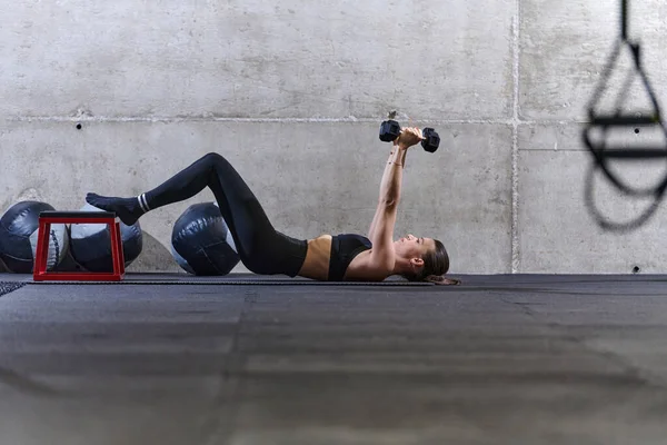 Zdolna Kobieta Leży Podłodze Sali Gimnastycznej Wykonując Ćwiczenia Ramion Hantlami — Zdjęcie stockowe