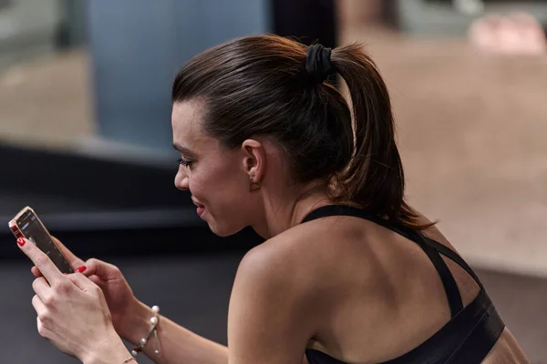 stock image A fit woman in the gym taking a break from her training and uses her smartphone, embracing the convenience of technology to stay connected.