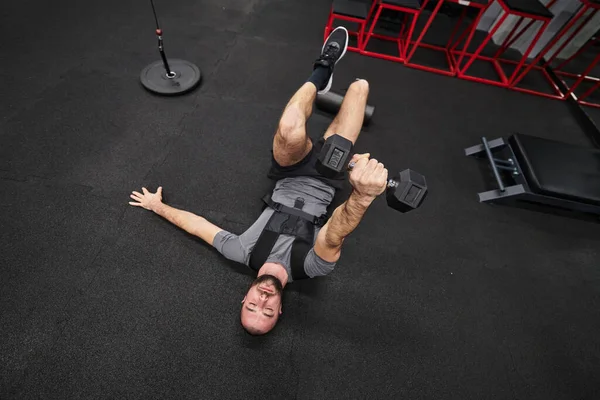 근육질의 남자가 현대적 체육관에서 덤벨을 가지고 운동하는 초점을 맞추고 — 스톡 사진