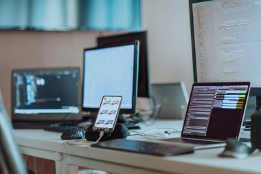 Boş yazılım geliştirme bürosunda programlama kodu çalıştıran bilgisayar ekranları ve arka plandaki veri algoritmalarını ayrıştıran bilgisayarlar. Veri odasında sinirsel ağ sunucuları bulut hesaplaması yapıyor. Yüksek
