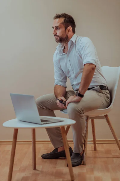 一位自信的商人坐在那里 使用带有坚定表情的笔记本电脑 而米色背景则提升了职业氛围 展示了他的生产力和专业知识 — 图库照片